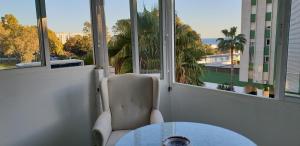 une chaise et une table dans une chambre avec fenêtres dans l'établissement Piso 110m² en el Palo con parking cerca de la playa, à Malaga
