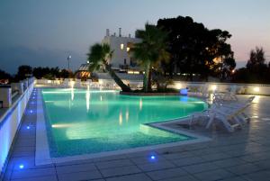 una piscina notturna con sedie e un albero di Hyencos Hotel Calos a Torre San Giovanni Ugento