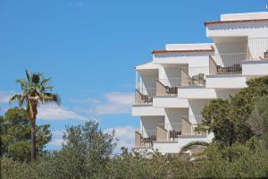 a white building with balconies and a palm tree at Aparthotel Niu d´Aus in Portopetro