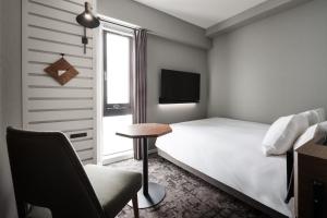 a bedroom with a bed and a chair and a television at Nest Hotel Hiroshima Hatchobori in Hiroshima