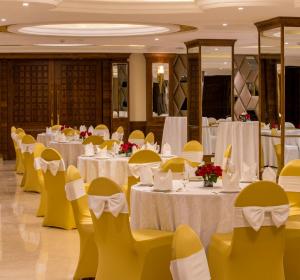 um salão de banquetes com mesas brancas e cadeiras amarelas em Regenta Central Cassia Zirakpur Chandigarh em Chandīgarh