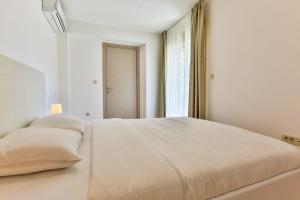 a white bedroom with a large bed with two pillows at Gufo Apart in Budva