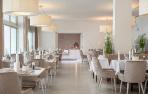uma sala de jantar com mesas e cadeiras brancas e janelas em Seehotel Europa em Velden am Wörthersee