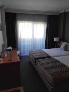 a hotel room with two beds and a desk and a window at Dom Joao Hotel in Entroncamento