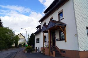 ein weißes Gebäude mit einer Veranda und einer Treppe auf einer Straße in der Unterkunft Eifelferienhaus Thome in Lissendorf