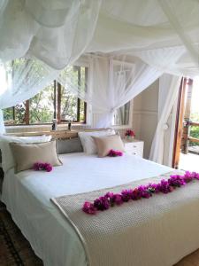 Una gran cama blanca con flores púrpuras. en Casa Karibu at Santa Maria Machangulo Mozambique, en Santa Maria