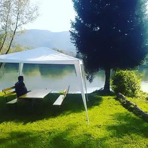 un homme assis sur un banc sous une tente à côté d'un lac dans l'établissement Kuća-Zvorničko jezero, à Mali Zvornik