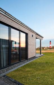 ein Haus mit großen Glasfenstern und einem Leuchtturm in der Unterkunft Gud Jard Lodge Nr 19 - Design-Ferienhaus mit exklusiver Ausstattung in Pellworm