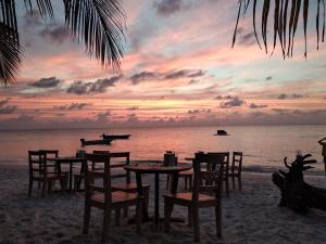 a table and chairs on the beach with a sunset at Dhigurah Beach Inn in Dhigurah