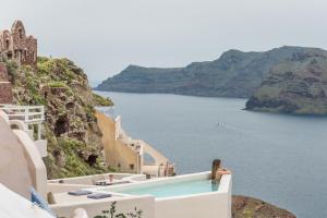 Una donna seduta sul bordo di una piscina che guarda l'oceano di Art Maisons Oia Castle a Oia