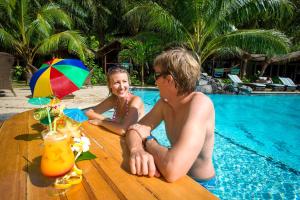 a man and a little girl sitting at a table by a pool at Seabreeze Resort Samoa – Exclusively for Adults in Aufaga