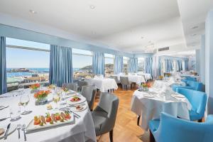 un restaurante con mesas y sillas blancas y ventanas en La Fregate Hotel en St. Peter Port