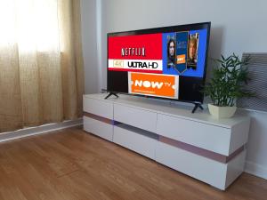 a television on a white dresser in a living room at 3 Bed Luxury Town Center Apartment with 50 inch 4K TV (Netflix & NowTV Ent. Pass) in Northampton