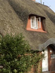 een huis met een rieten dak en een raam bij Marschküken in Wrixum