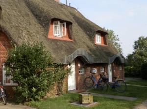 una casa con techo de paja y 2 bicicletas estacionadas fuera en Marschküken, en Wrixum