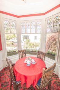 a dining room with a red table with chairs and windows at Elim Bank Guest House in Bowness-on-Windermere
