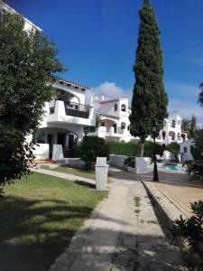 une grande maison blanche avec un arbre en face dans l'établissement Siesta mar 2, à Cala'n Porter