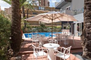 eine Terrasse mit Tischen, Stühlen und einem Sonnenschirm in der Unterkunft Hotel El Palmeral in Benidorm
