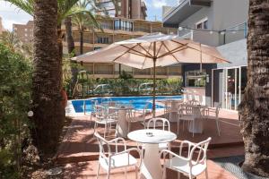 een patio met tafels en stoelen en een parasol bij Hotel El Palmeral in Benidorm