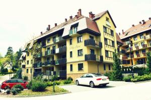 une voiture blanche garée devant un grand bâtiment dans l'établissement Apartamenty Polanica Zdrój, à Polanica-Zdrój
