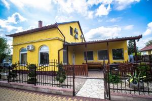 a yellow house with a fence in front of it at Mickey's Thermal Apartments in Tiszakécske