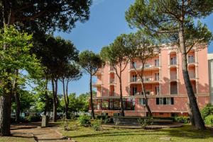 różowy budynek z drzewami przed nim w obiekcie Hotel Corallo w mieście Misano Adriatico