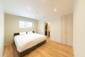 a bedroom with a large white bed and wooden floors at Black Crane Chalet by Hakuba White Fox Company in Hakuba