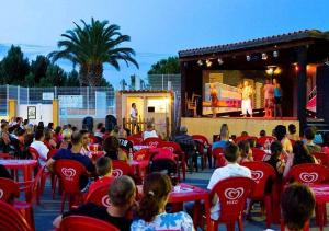 a crowd of people sitting in red chairs in front of a stage at les cigales in Vic-la-Gardiole