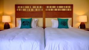 two beds with white sheets and blue pillows at The Uza Terrace Beach Club Villas in Yomitan