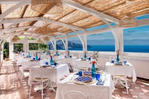 a dining room with white tables and chairs and the ocean at Gocce Di Capri Resort in Massa Lubrense