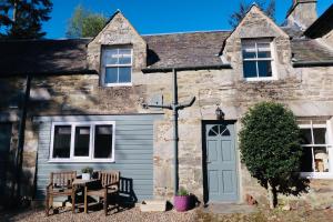 an old stone house with a table and chairs in front of it at Red Squirrel Cottage in Strathtay