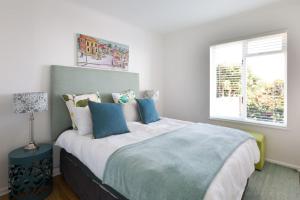 a white bedroom with a large bed with blue pillows at Watercolours Studios in Simonʼs Town