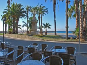 a row of tables and chairs with palm trees and the beach at Hotel Celimar in Sitges