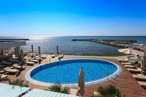 Carmen International Hotel Venus - Fost Becali Hotel في فينوس: مسبح وكراسي ومظلات بجوار المحيط