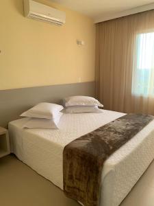 Dunamys Hotel Londrina في لوندرينا: غرفة نوم بسرير كبير عليها شراشف ووسائد بيضاء