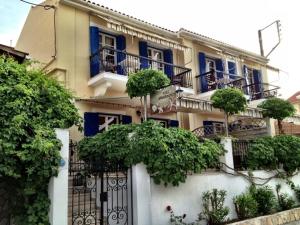 a building with blue windows and a gate with trees at Kiki Studios in Fiskardo