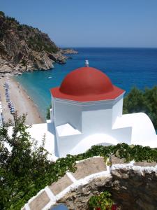 a lighthouse with a red roof on a beach at Roses Studios in Karpathos