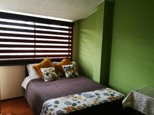 a bedroom with a bed with green walls and a window at Chapelet Hostal in Tababela