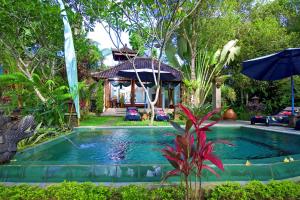 a swimming pool with an umbrella and a house at The Mahogany Villa in Tegalalang