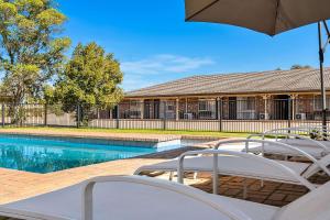 a swimming pool with two chairs and an umbrella at Quality Inn Carriage House in Wagga Wagga