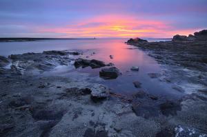 a sunset on a beach with rocks and water at 103 Boutique Hotel Stintino in Stintino