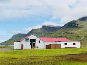 a white barn in a field with mountains in the background at Óseyri Hlaðan -The Barn studio apartment in Stöðvarfjörður