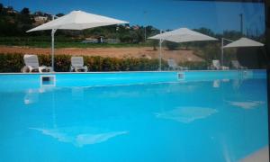 a blue swimming pool with two umbrellas and two chairs at Il Casale Delle Rose in Caltagirone