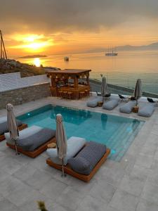 a pool with lounge chairs and a table and the ocean at Apiro Mykonos in Mýkonos City