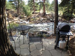 a grill and two tables and chairs next to a river at Swiftcurrent Lodge in Estes Park
