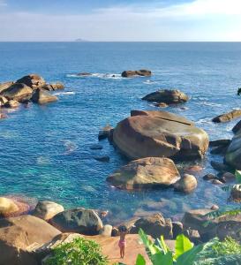 a person standing in the water on a rocky beach at Vila Pequeá Ilhabela in Ilhabela