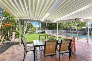 a patio with a table and chairs under a pergola at Clouds End in Noosaville