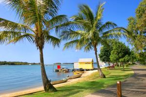 a beach with palm trees and a yellow house at Clouds End in Noosaville