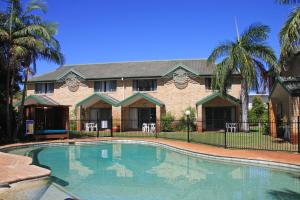 a swimming pool in front of a house with palm trees at Aqua Villa Holiday Apartments in Coffs Harbour