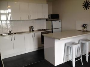 a kitchen with white cabinets and a counter and stools at Accommodation Portland Victoria in Portland